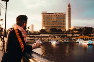 Kahire Mısır Aralık 2021 Kahire Mısırında Zamalek bölgesine uzanan bir köprünün çitine yaslanan Kahire Kulesi. Nil nehri zarif bir şekilde akıp giden gemilerle