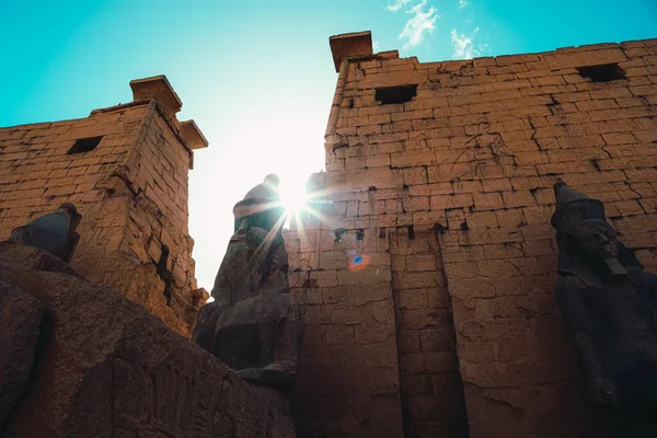 エジプトの古代の豪華な寺院への入り口 明るいエジプトの太陽に照らされた巨大な石の壁 太陽が巨大な古代の像の頭の中を歩く — ストック写真