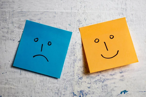 Happy and sad faces hand drawn on sticky notes on painted wall