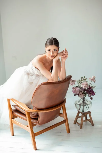 Porträt eines schönen Mädchens im Hochzeitskleid. Braut im luxuriösen Kleid sitzt auf dem Stuhl — Stockfoto