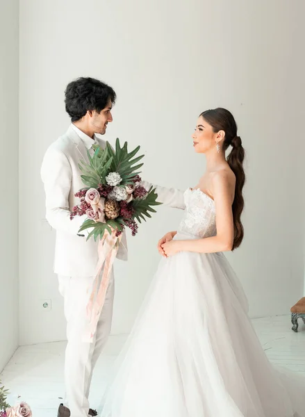 Bride in white dress and groom in suit, posing in white Studio — Stock Photo, Image