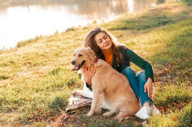 Gülümseyen bir kadın köpeğine sarılıyor. Golden Retriever köpeği, güneşli bir günde dışarıda yürüyen kıvırcık bir kadınla oynuyor. Sevgi ve evcil hayvan için bakım.