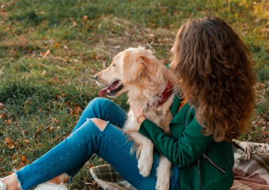 Parkta köpeğine sarılan kıvırcık bir genç kadının portresi. Genç kıvırcık kadın sonbahar yapraklarında köpeğiyle oturuyor.