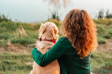 Güneşli bir günde dışarıda gezen kıvırcık bir kadınla Golden Retriever köpeği. Parkta köpeği eğitiyorum. Evcil hayvana sevgi ve ilgi göster. Arka plan