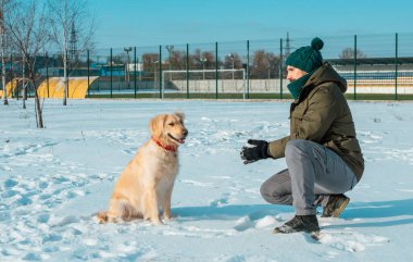 Genç bir adam kış günü elinden kar tanelerini Golden Retriever köpeğine üflüyor. Dostluk, evcil hayvan ve insan.