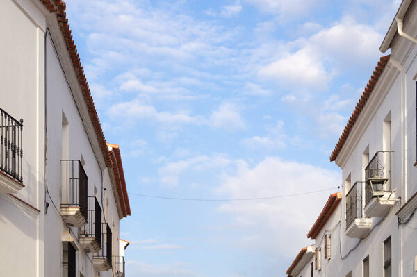 Artistic image of two building facades with white walls and a beautiful blue sky with clouds in the background conveying tranquillity. Top floors of two small buildings in a village on a sunny day.
