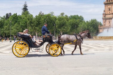 Plaza de Espana çevresinde at arabasıyla (Seville, Endülüs) dolaşan yaşlı bir çift. Güneşli bir günde şehrin turistik bir bölgesinde at arabasında oturan turist çift..