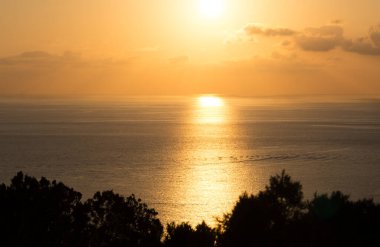 Güneşin denizin gerisinde battığı altın saatte güzel bir gün batımı. Güneşin denizdeki yansıması. Arkaplanda deniz ve suyu aydınlatan güneş ile sonsuzluğa bakıyor..