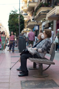 Two old women sitting on a bench looking straight ahead as people pass around them. Two elderly women sitting on a bench to rest. Concept of solitude.