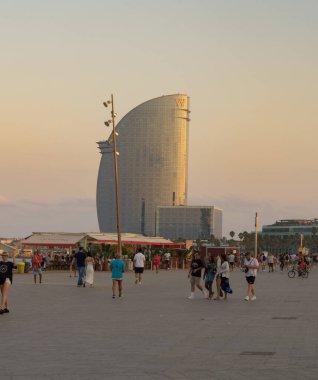 İnsanlar gün batımında Barselona 'nın arka planında ünlü W Barselona otelinde geziniyorlar (Katalonya, İspanya).
