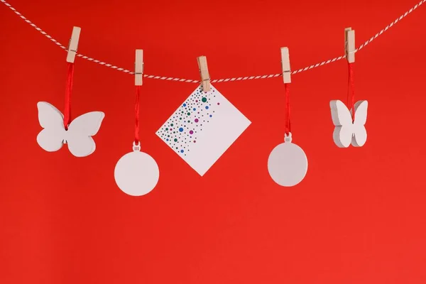 Yazı için yeri olan bembeyaz beş Noel süsü. Kırmızı arkaplandaki yazı için süslemeler ve yazıtlar. Mandallı bir ipe tebrikler asma geleneği.