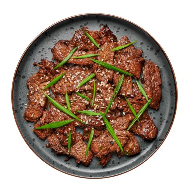 Beef Bulgogi on black plate isolated on white. Korean cuisine meat dish with sauce and kiwi. Traditional asian food. Top view