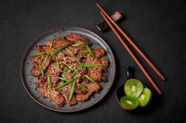 Beef Bulgogi on black plate on dark slate table top. Korean cuisine meat dish with sauce and kiwi. Traditional asian food