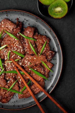 Beef Bulgogi on black plate on dark slate table top. Korean cuisine meat dish with sauce and kiwi. Traditional asian food. Top view