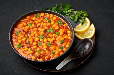 Chana Masala or Chole in black bowl on dark slate table top. Indian cuisine veg chickpeas curry dish. Asian spicy vegetarian food and meal.