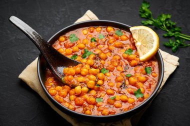 Chana Masala or Chole in black bowl on dark slate table top. Indian cuisine veg chickpeas curry dish. Asian spicy vegetarian food and meal. Close up