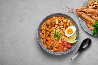 Laksa in gray bowl on concrete table top. Coconut noodle soup with chicken meat and prawns of peranakan cuisine. Asian food.