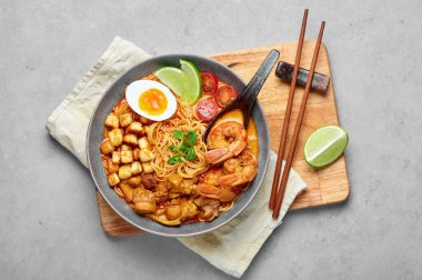 Laksa in gray bowl on concrete table top. Coconut noodle soup with chicken meat and prawns of peranakan cuisine. Asian food.