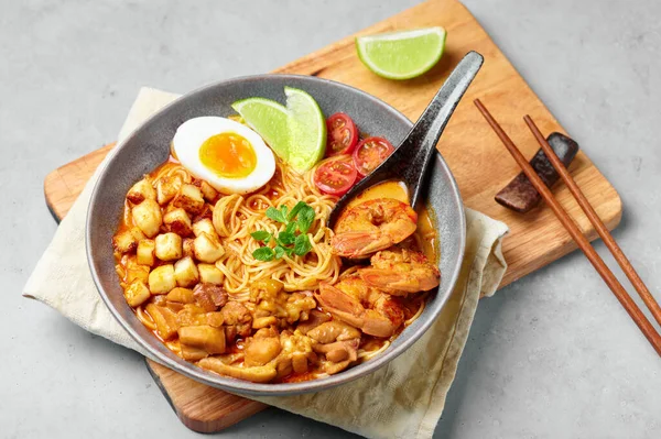 Laksa in gray bowl on concrete table top. Coconut noodle soup with chicken meat and prawns of peranakan cuisine. Asian food.