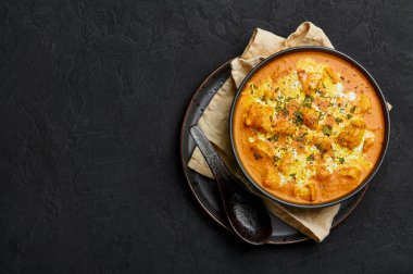 Murgh Makhani or Butter Chicken in black bowl on dark slate table top. Indian Cuisine dish with chicken meat and creamy masala. Asian food and meal. Copy space. Top view