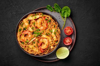 Mie Goreng in black bowl on dark slate table top. Indonesian cuisine prawn noodles and vegetables stir fired dish. Asian food. Top view