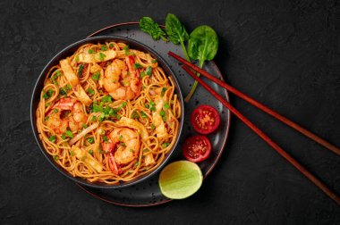 Mie Goreng in black bowl on dark slate table top. Indonesian cuisine prawn noodles and vegetables stir fired dish. Asian food. Top view