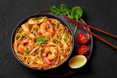 Mie Goreng in black bowl on dark slate table top. Indonesian cuisine prawn noodles and vegetables stir fired dish. Asian food.