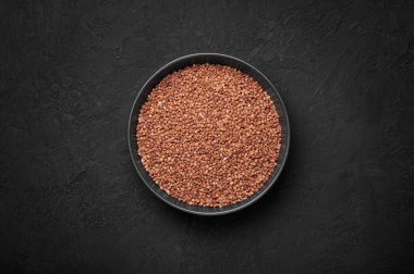 Raw buckwheat groats in black bowl on dark slate table top. Healthy vegetarian organic food ingredient