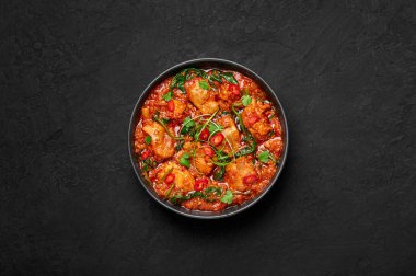 Chicken Vindaloo with spinach in black bowl on dark slate table top. Indian cuisine meat chilli curry dish. Authentic asian food. Top view