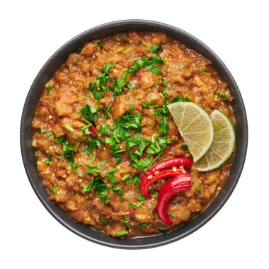 Baingan Bharta or Roasted Mashed Eggplant in black bowl isolated on white background. Bhurta is indian cuisine puree dish of fire roasted eggplant and masala. Top view