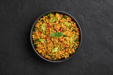 Masala Egg Bhurji or Muttai Podimas in black bowl on dark slate table top. Anda Bhurji is indian cuisine scrambled eggs dish with spices. Asian food and meal. Top view