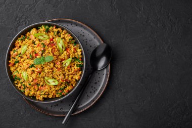 Masala Egg Bhurji or Muttai Podimas in black bowl on dark slate table top. Anda Bhurji is indian cuisine scrambled eggs dish with spices. Asian food and meal. Copy space