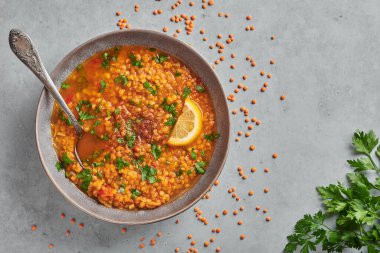 Red lentils tomato soup with parsley and lemon in gray plate on concrete table top. Vegetarian dish. Copy space