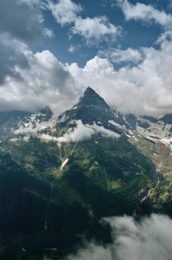 Sharp mountain peak landscape with cloudy sky, rocky ranges and peaks with glaciers and snow fields. Wild nature view. Belalakaya, Dombay, Caucasus