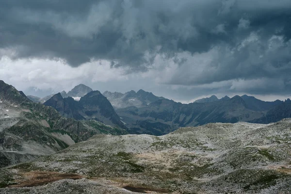 Gloomy mountain landscape with thunder cloudy sky, rocky ranges and peaks with glaciers and snow fields. Wild nature valley