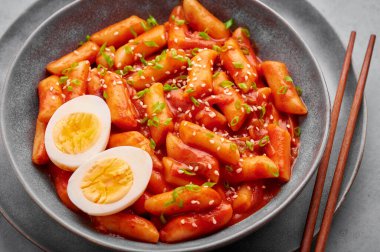 Tteokbokki with eggs in gray bowl on concrete table top. Tteok-bokki is a korean cuisine dish with rice cakes. Asian food.