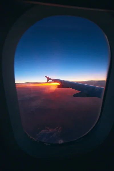 Beautiful sunrise view through the porthole during the flight. Plane wing above the cloudy colorful sunset