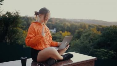 Parkta oturan gözlüklü ve turuncu bluzlu öğrenci yurt dışında ailesiyle görüntülü konuşma yapıyor. Onları gülümseyerek selamladı, elini salladı. Alıcı konsepti. 4k konsepti