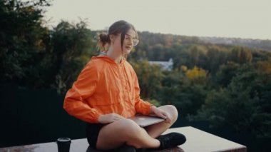 Azimli öğrenci projeyi bitirir, dizüstü bilgisayarı kapatır ve rahatlamak için boynuyla dairesel hareketler yapar. Parlak turuncu bir bluz giymişti. Saçları topuz şeklindeydi.