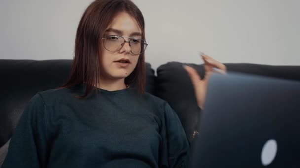 Mujer pelirroja con gafas, freelancer que enseña un entrenamiento en línea. Vestido con una blusa verde oscuro, sentado en un sofá negro. El concepto de la mujer trabajadora. Concepto 4k — Vídeos de Stock