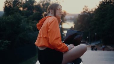 Düşünceli ve yorgun genç bir kadın gözlüklerini yerleştirir ve kafasını avucuna koyar. Parlak turuncu bir bluz giymiş, saçı topuz şeklinde, park şeridinde konumlanmış. 4k konsepti