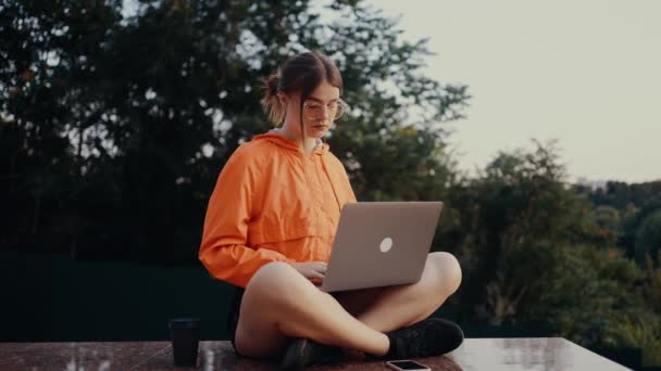 The young worker, optimistic who works concentrated in the park then raises her head and displays a wide smile. Dressed in a bright orange blouse, hair caught in a bun, in the lotus position on the — Stock Video