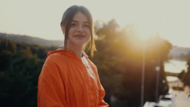 Kızıl saçlı ve çilli kız, parkın girişinde oturuyor, doğrudan kameranın önüne bakıyor. Turuncu bir bluz giymişti. Doğadaki insan kavramı. 4k konsepti