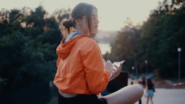 The ambitious young woman, freelancer, is working on a new project, making notes in her notebook. Dressed in a bright orange blouse, hair caught in a bun, positioned on the park strip. 4k concept
