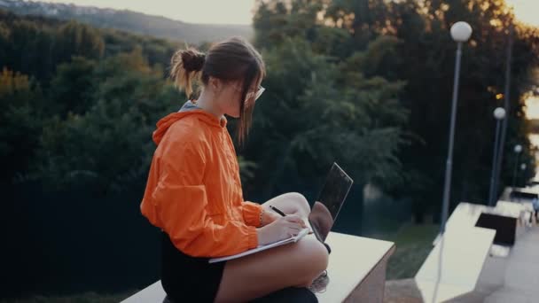 Mujer joven planeando sus acciones para la próxima semana laboral. Vestido con una blusa naranja brillante, pelo atrapado en un moño, en el fondo del bosque verde y denso. Concepto 4k — Vídeos de Stock