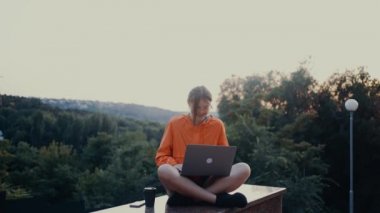 Parkta yoğunlaşmış, iyimser çalışan genç işçi başını kaldırıp geniş bir gülümseme sergiliyor. Parlak turuncu bir bluz giymişti. Saçları topuz şeklindeydi. Lotus pozisyonundaydı.