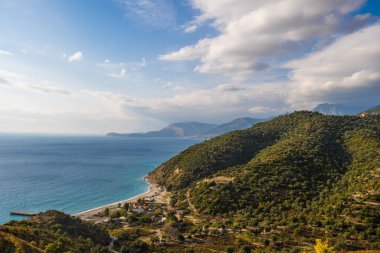 Önünde zeytin ağaçları ve çimenler olan küçük bir dağın tepesinden deniz manzarası