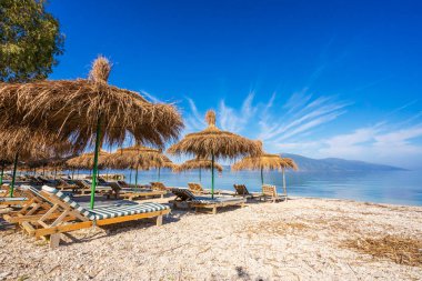 Deniz kıyısı, deniz ve gökyüzünün arka planında şemsiyeleri ve güneşlikleri olan kumsal.