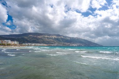 Bulutlu mavi gökyüzünde parlak mavi okyanus ufukta citi var.