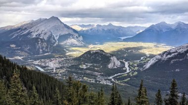 Alberta 'daki Sülfür Dağı' nın tepesinden Banff kasabasının manzarası. Bulutlu bir günde, güneş bulutların arasından ışıldar ve yakındaki araziyi aydınlatır. Gölgelerde ve renklerde zıtlıklar yaratır..